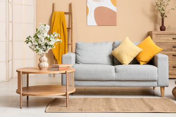 Sofa with dresser, coffee table and vase of white blooming branches near beige wall in living room