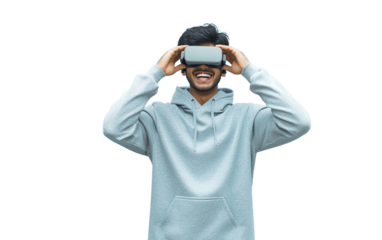 Excited Indian young man in gray hoodie holding VR headset near his eyes, isolated on pastel background, perfect for tech, virtual reality, or playful moments.

