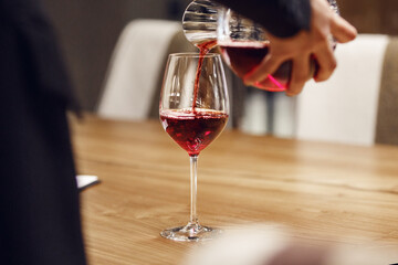 Bartender pouring red wine from decanter to the glass, close up image.