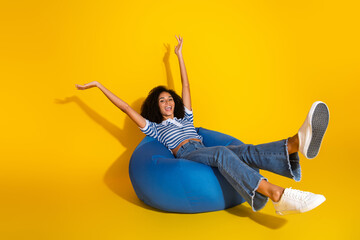 Young woman enjoying leisure time sitting on a funky blue bean bag chair against a vibrant yellow...