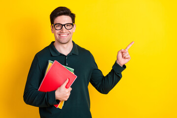 Young man in green polo holding notebooks while pointing to the side against a vibrant yellow...