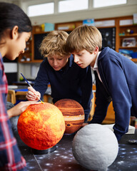 Fototapeta premium young students collaborating on creation of styrofoam solar system model, applying paint to Mars sphere, classroom learning environment