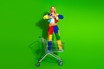 Fashionable young woman posing in bright colorful outfit on green background, playful and trendy...