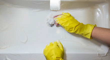 A girl washes and cleans the sink with a cleaning agent wearing yellow rubber gloves. Whitening and shine product, close-up. Copy space for text
