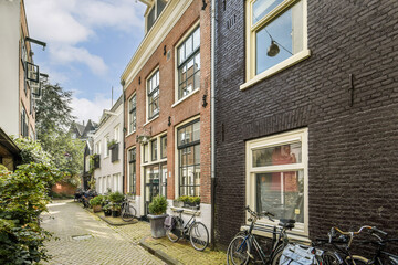 A picturesque view of a narrow street in Amsterdam lined with vintage buildings and bicycles. The lush greenery adds to the serene charm of the surroundings.