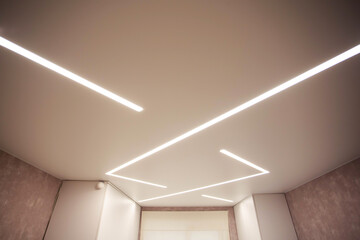 Modern designer stretch ceiling with illuminated LED lines in the room, backlighting