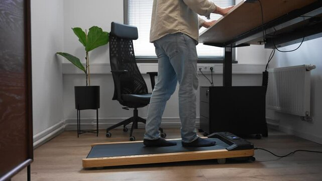 Standing and walking at adjustable desk with compact treadmill in stylish minimalist home office &ndash; promoting movement and productivity during remote work