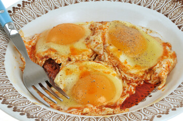 Œufs au plat sauce soubressade servis dans une assiette avec une fourchette en gros plan