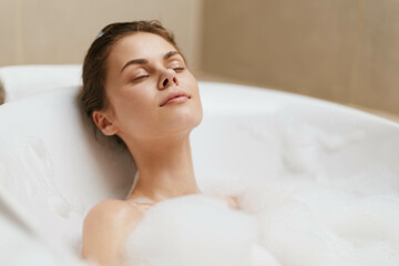 Relaxed woman enjoying a bubble bath in a modern bathroom, closed eyes and serene expression....