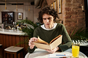 Handsome young man enjoys leisure reading at a cozy cafe while sipping fresh juice