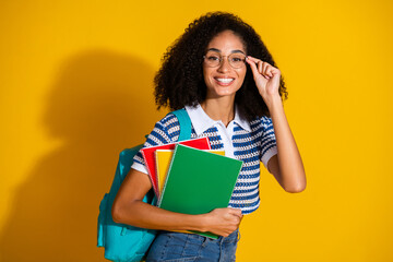 Cheerful young woman wearing glasses and a striped shirt holding notebooks with a vibrant yellow...