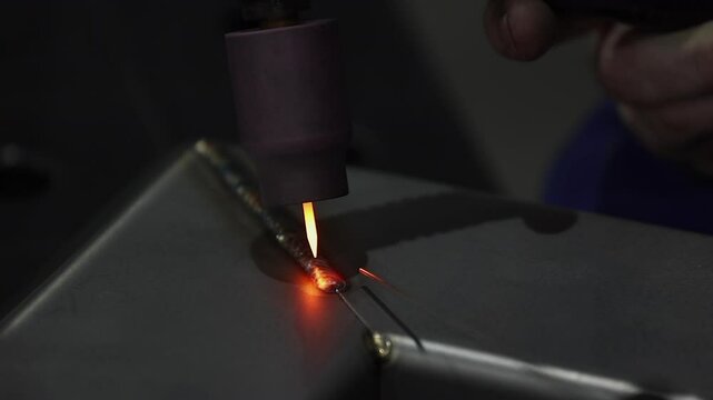 Close up: Welder inspects corner weld by glow of TIG welder electrode