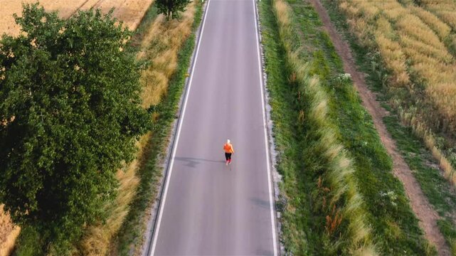 Young blonde woman doing a morning run on an empty road in a village in Baden Wurttemberg, Germany. Aerial view of a woman running at sunrise on a countryside road
