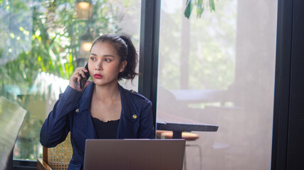 Asian businesswoman holding phone to ear and discussing business with partner and colleagues. Serious woman working remote in a cafe