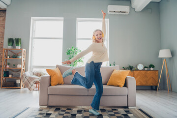 Young woman joyfully dancing in a cozy living room with modern interior design and natural daylight...