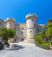A sunny, low-angle shot captures the stone facade and round towers of the Palace of the Grand...