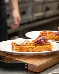 Chef preparing waffle with brisket and cheese in cafe kitchen