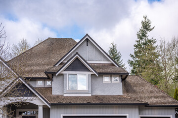 Top of grey stucco luxury house with shingle roof, trees and nice windows in Spring in Vancouver, Canada, North America. Day time on April 2025.