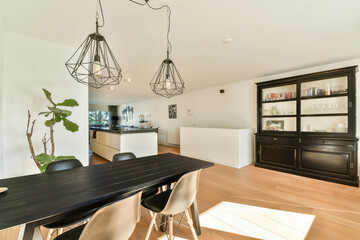 A bright and airy dining room featuring a sleek black table and stylish pendant lights. Green plants enhance the modern aesthetic of the interior design.