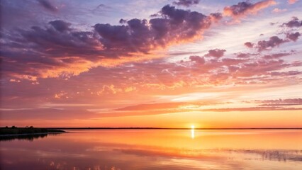 Obraz premium Vibrant sunset over calm lake with reflections of sky and clouds in water