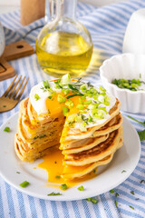 Tasty savory breakfast pancakes with spring green onion and fried eggs. Stack or delicious non-sweet pancakes with scallons, parsley and sunny side up eggs, on white kitchen table copy space