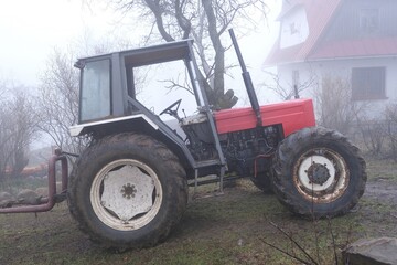 Very misty scenery tractor standing next to building in village.