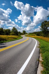 Winding road leads through countryside, trees on the sides and cloudy sky above