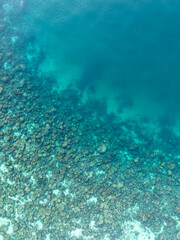 Aerial view of a coral reef fringing deeper blue waters in a tropical sea. The image highlights the natural gradient from shallow reef to open ocean.