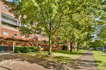 Obraz premium A vibrant park scene showcasing lush green trees and well-kept paths alongside modern residential buildings, perfect for community relaxation and outdoor activities.