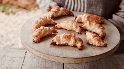 Artisan Baker Holding Freshly Baked Mini Croissants on Rustic Board.
