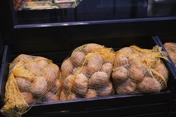 Several large mesh bags filled with raw potatoes are stacked in a storage bin, ready for use in a...