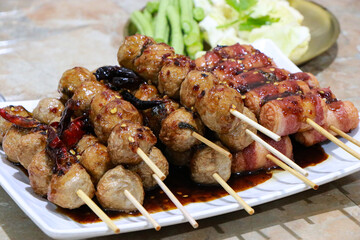 Grilled Meatballs. fish ball and sausage hotdog grilled in stick on tray, Fried pork meatballs skewers bamboo on a white plate with spicy sauce on a table, Thai street food.