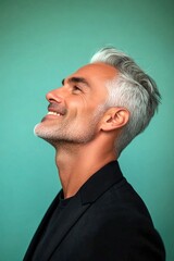 Fototapeta premium Green solid background. Visual idea of style for aging men. Classy men's short caesar haircut - midlife white man with white hair. A cheerful and glowing gentleman with a relaxed demeanor.