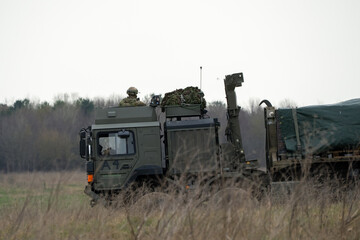 Soldier lookout in the cab of British army MAN SV HX 8x8 eight wheeled logistics truck carrying supplies across countryside