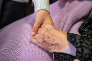 Young child's hand gently holds the wrinkled hand of an elderly woman, conveying love, care, and intergenerational connection in a heartwarming moment of support and affection
