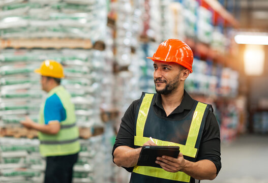 caucasian warehouse worker checking using tablet. caucasian man wearing safety examine storage area with touch screen document. supervisor wear helmet safety vest at workplace inspect stock by tablet