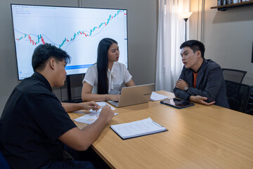 Group discusses financial strategies in modern office setting with market trends displayed on screen
