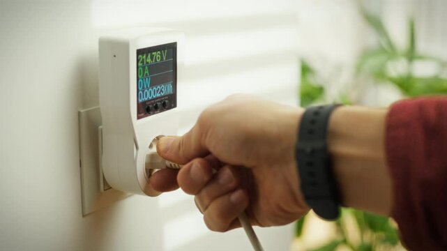 A person is connecting an electrical plug into an energy monitor at home. This action highlights the importance of tracking energy usage for better efficiency and conservation