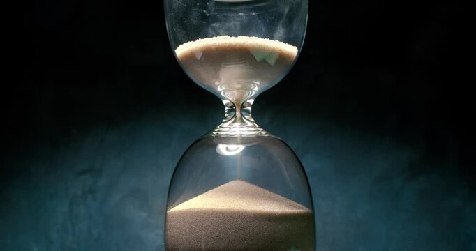 Hourglass with grains of sand on a dark background. Shot on super slow motion camera 1000 fps.