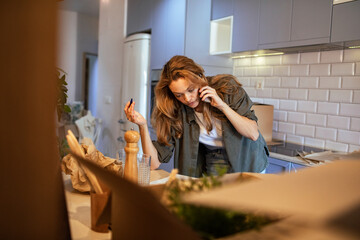 Busy woman talking on smartphone during home unpacking in kitchen