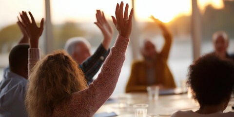 A diverse group of people is seen in a meeting, raising their hands to participate in discussion, highlighting community engagement and collaboration in a warm ambiance.