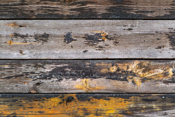 Fototapeta premium The photo shows old, damaged wooden boards with visible signs of wear, discoloration and yellow paint stains. The wood texture and color contrast give the photo a rustic, raw character