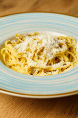 Classic spaghetti cacio e pepe with grated cheese on a blue-striped plate