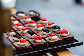 Catering service offering small brownies decorated with cream and berries
