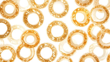 Close-up shot of numerous golden, sparkly, ring-shaped candies against a white background. The...