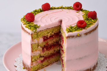 layered Raspberry Pistachio Cake frosted with light pink cream and garnished with fresh raspberries and chopped pistachios closeup side view of classic delicious dessert