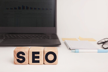 Wooden blocks spelling “SEO” are placed in focus on a tidy workspace. A laptop, notepad, pen, and sticky notes sit in the blurred background. Ideal for illustrating digital marketing or SEO articles.