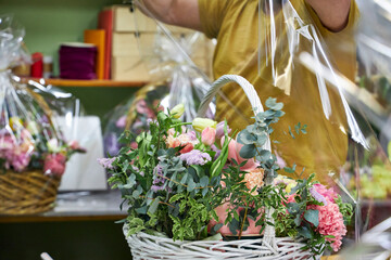 a male florist in a yellow T-shirt packs a large basket of flowers in the workshop