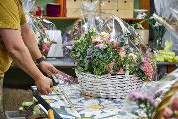 a male florist in a yellow T-shirt packs a large basket of flowers in the workshop