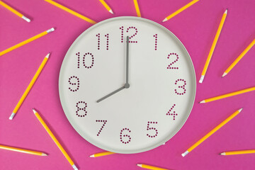 Eight o’clock on round wall clock And orange pencils on pink background. Flat lay clock showing...